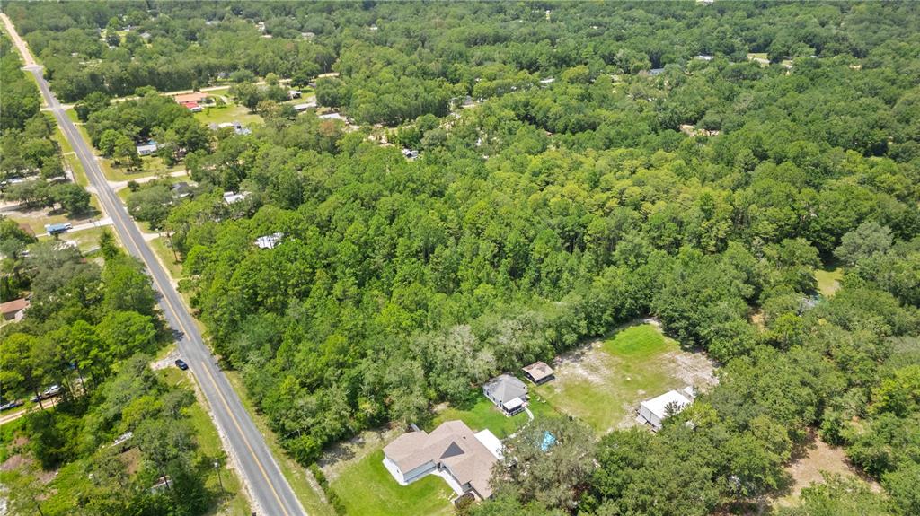 An aerial view shows a house with a pool and outbuildings surrounded by dense forest — 150 SESAME STREET, MIDDLEBURG, FL