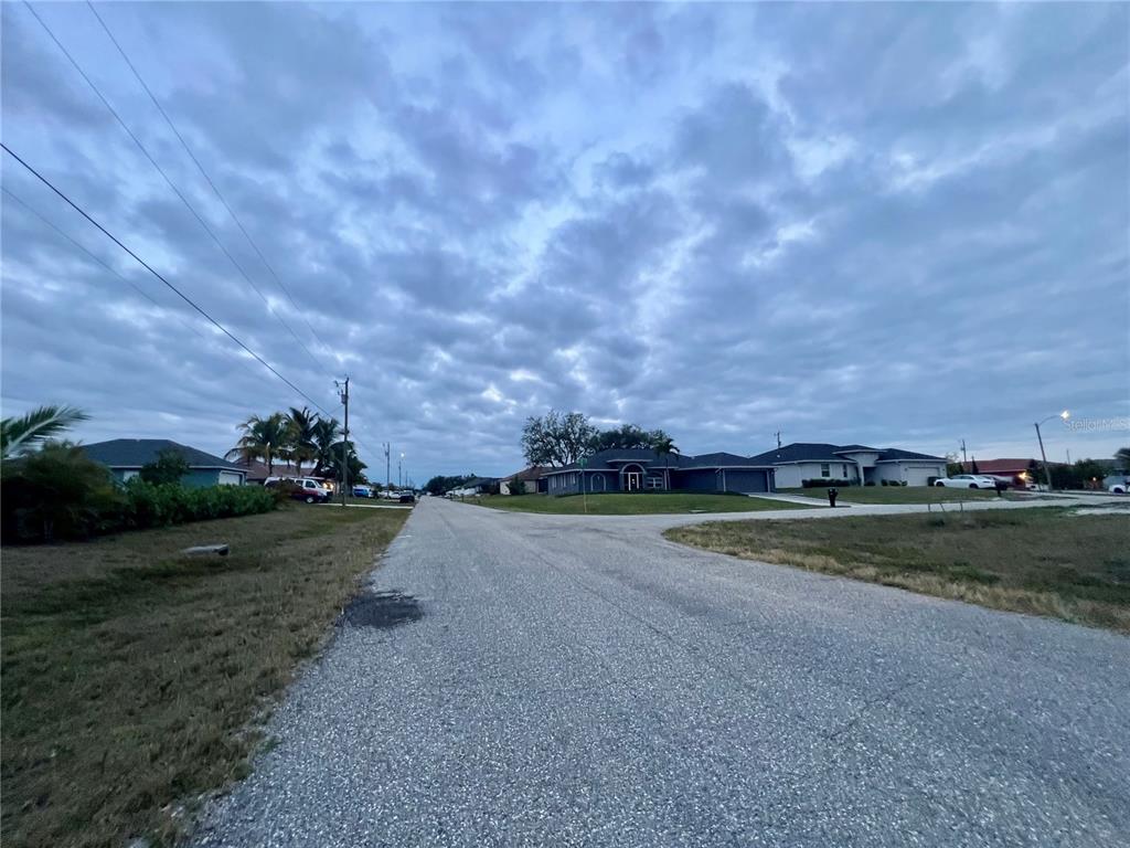A paved residential street leads toward houses under a cloudy sky — 1903 NE 10TH AVENUE, CAPE CORAL, FL
