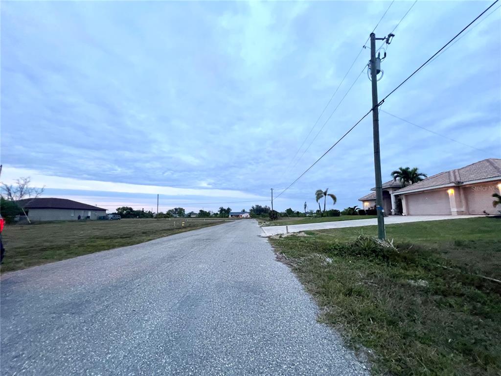 A paved road runs through a residential area with vacant lots and a nearby house — 1903 NE 10TH AVENUE, CAPE CORAL, FL