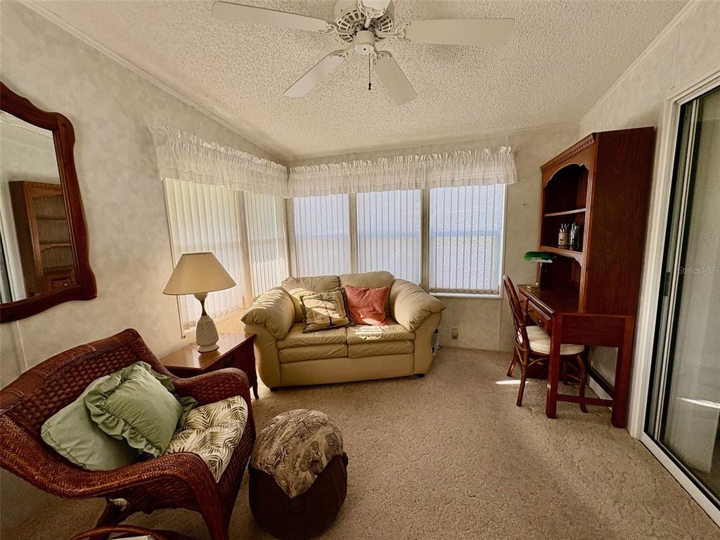 A sunroom features a beige loveseat, a wicker chair, a wooden desk, and carpeted flooring — 6133 GRAND OAKS DRIVE SE, WINTER HAVEN, FL