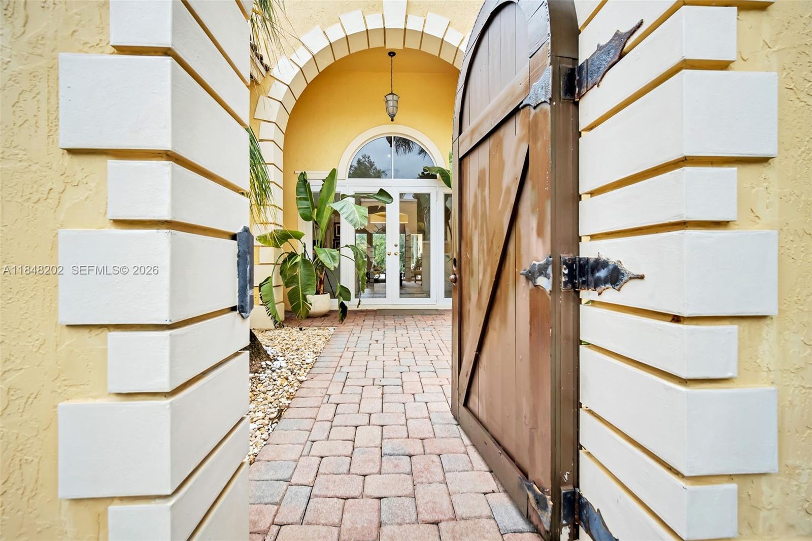 An arched wooden gate opens to a brick walkway leading to a glass-paned entryway — 14211 Sunset Ln, Southwest Ranches FL 33330, SOUTHWEST RANCHES, FL
