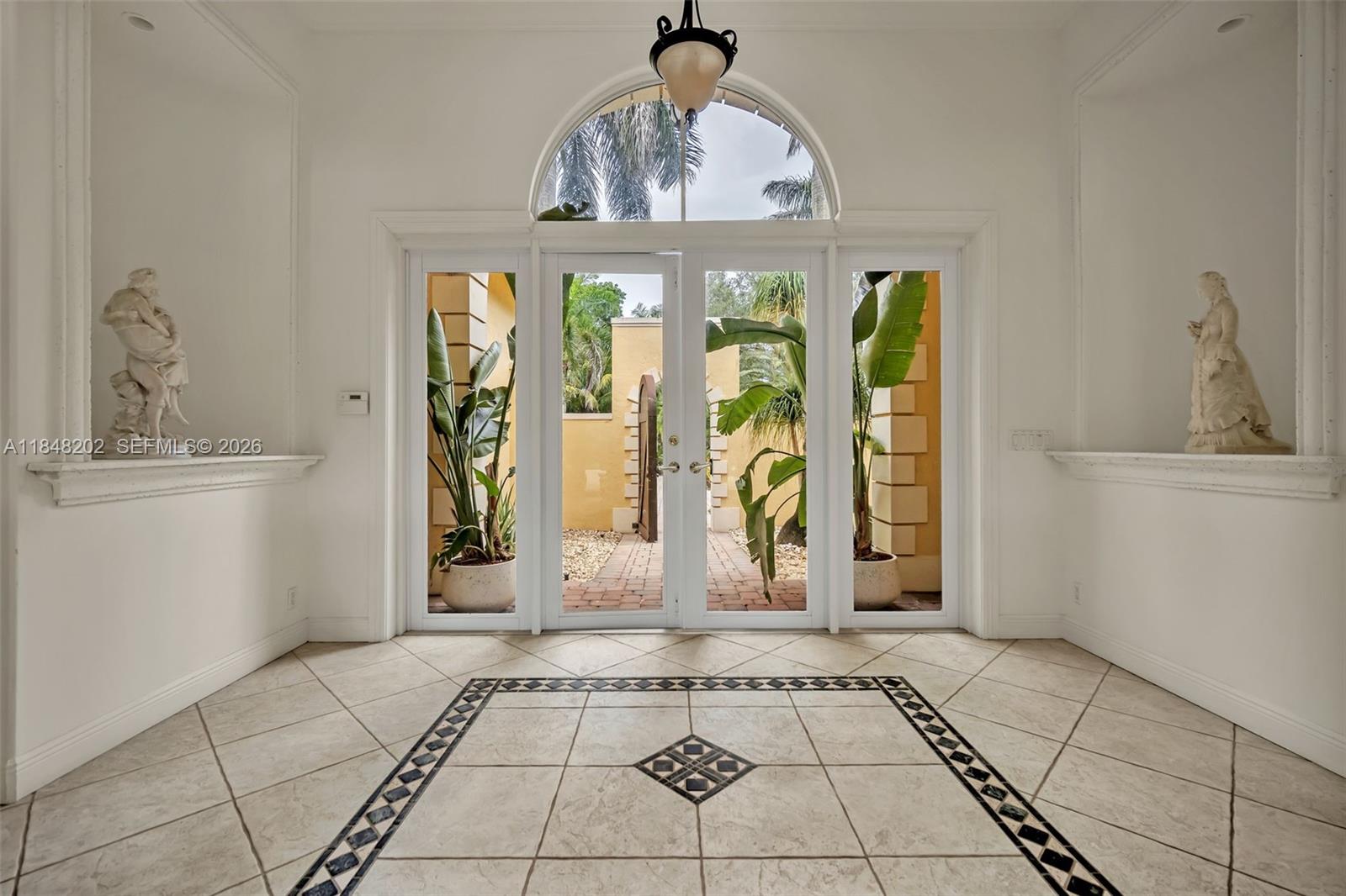 An entryway features tiled floors, dual statues in niches, and glass doors opening to a courtyard — 14211 Sunset Ln, Southwest Ranches FL 33330, SOUTHWEST RANCHES, FL