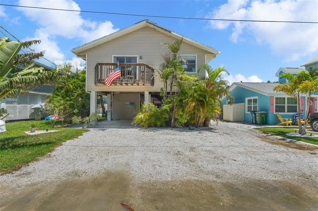 A two-story stilt house with a gravel driveway and a wooden balcony under a blue sky — 2517 AVENUE C, BRADENTON BEACH, FL