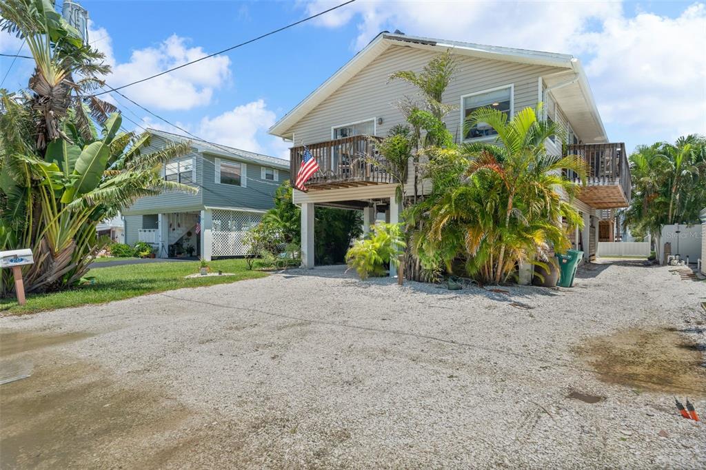 An elevated house with a gravel driveway, wooden balconies, and palm trees under a blue sky — 2517 AVENUE C, BRADENTON BEACH, FL