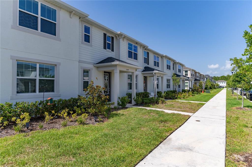 A row of two-story townhouses with light-colored siding and stucco exteriors sits beside a sidewalk — 11549 STRAITS WAY, ORLANDO, FL