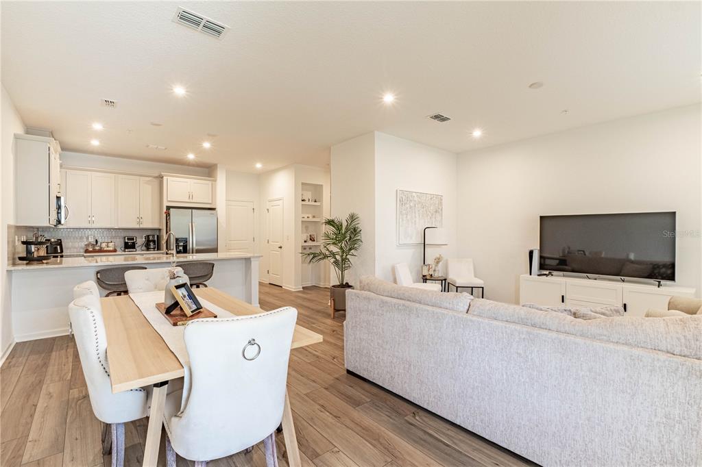 An open-concept living and dining area features light wood flooring and white kitchen cabinetry — 11549 STRAITS WAY, ORLANDO, FL