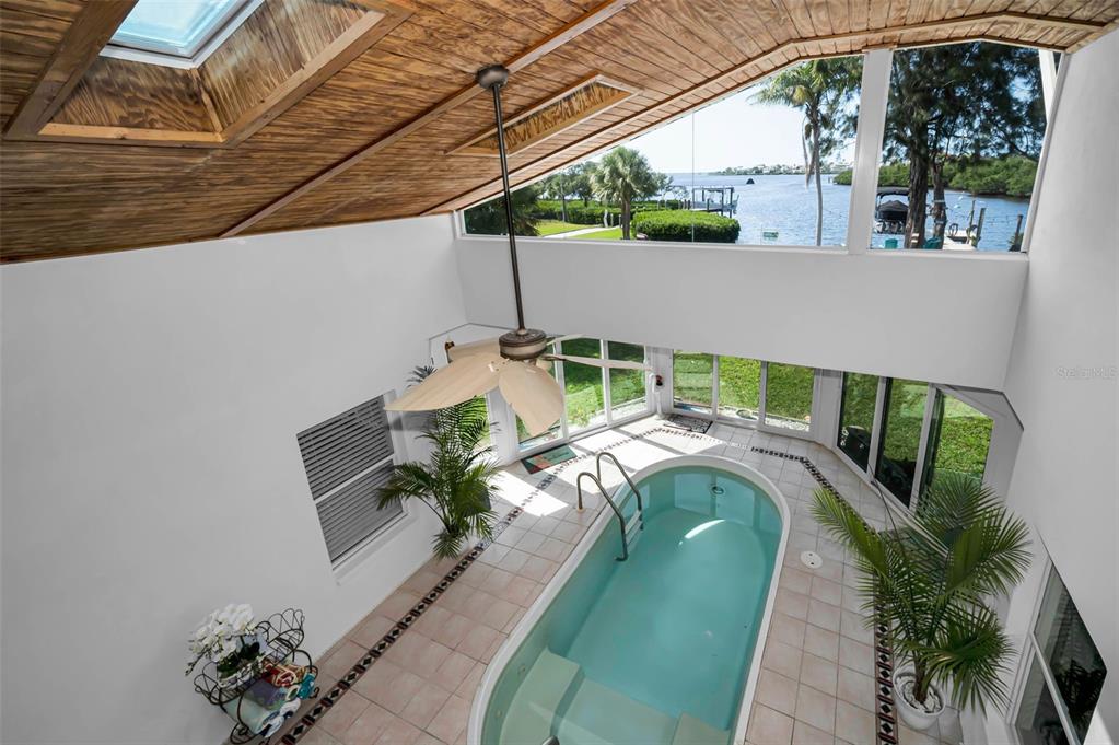 An indoor pool room features a vaulted wood ceiling, skylights, and large windows overlooking water — 1626 SEA BREEZE DRIVE, TARPON SPRINGS, FL