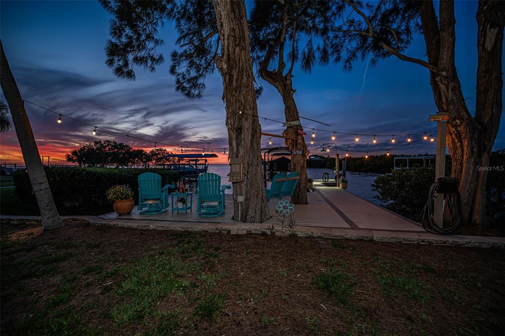 A wooden dock with turquoise chairs extends into the water under string lights at sunset — 1626 SEA BREEZE DRIVE, TARPON SPRINGS, FL