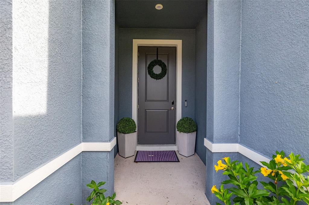 A gray front door with a wreath is flanked by two potted plants — 367 AUGUST FERN LOOP, MOUNT DORA, FL