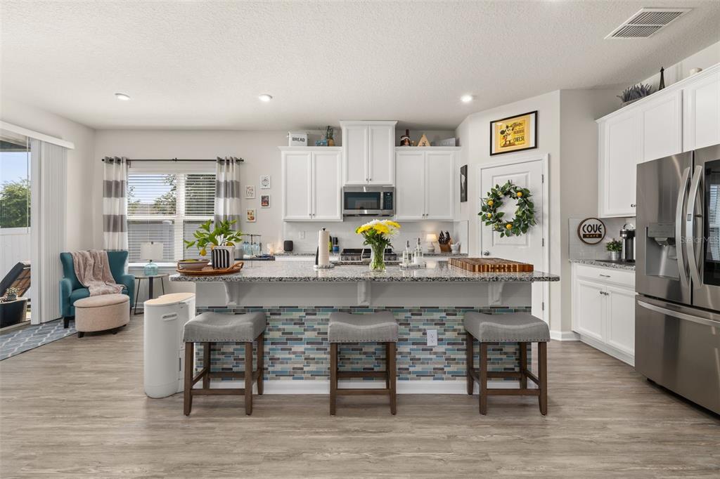A kitchen features a granite-topped island with blue tile accents and three gray bar stools — 367 AUGUST FERN LOOP, MOUNT DORA, FL