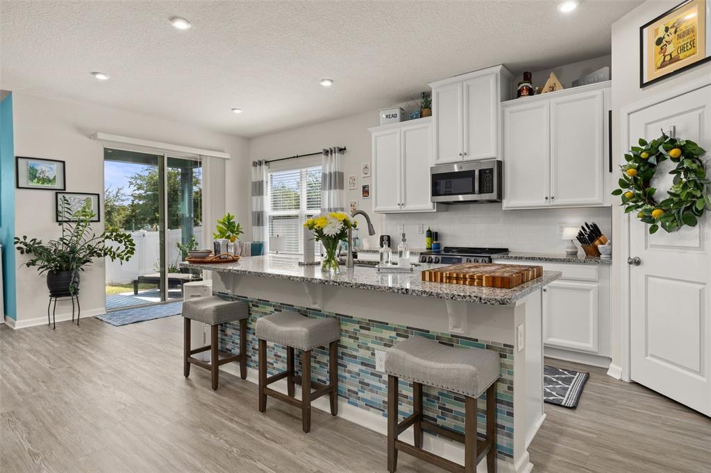 A kitchen features a granite-topped island with blue tile accents, white cabinetry, and sliding glass doors — 367 AUGUST FERN LOOP, MOUNT DORA, FL