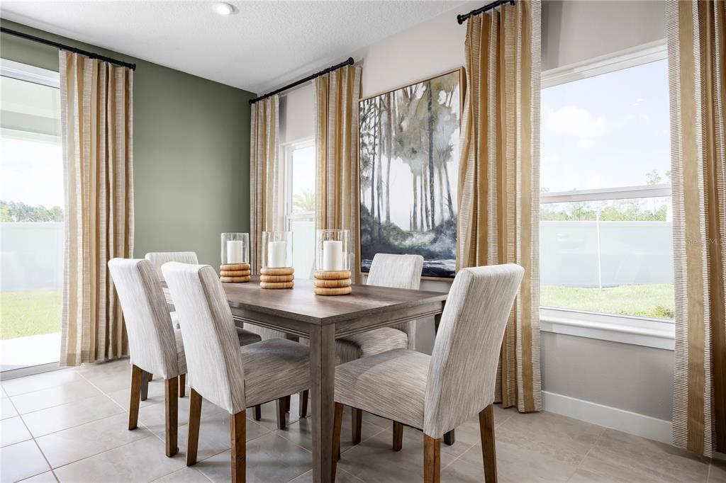 A dining room features a wooden table, upholstered chairs, large windows, and forest-themed wall art — 1676 SWEET SAPLING COURT, DAVENPORT, FL