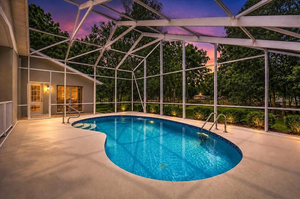 A kidney-shaped swimming pool sits inside a screened-in patio enclosure at sunset — 855 NW 75TH TERRACE, OCALA, FL