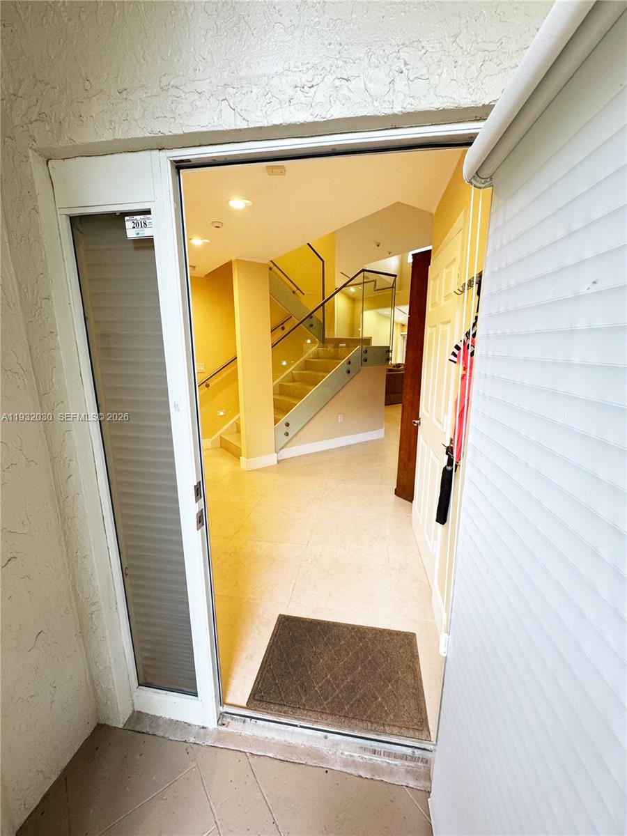 A view through an open doorway reveals a tiled entryway with a glass-railed staircase — 610 Misty Oaks Ln, Pompano Beach FL 33069, POMPANO BEACH, FL