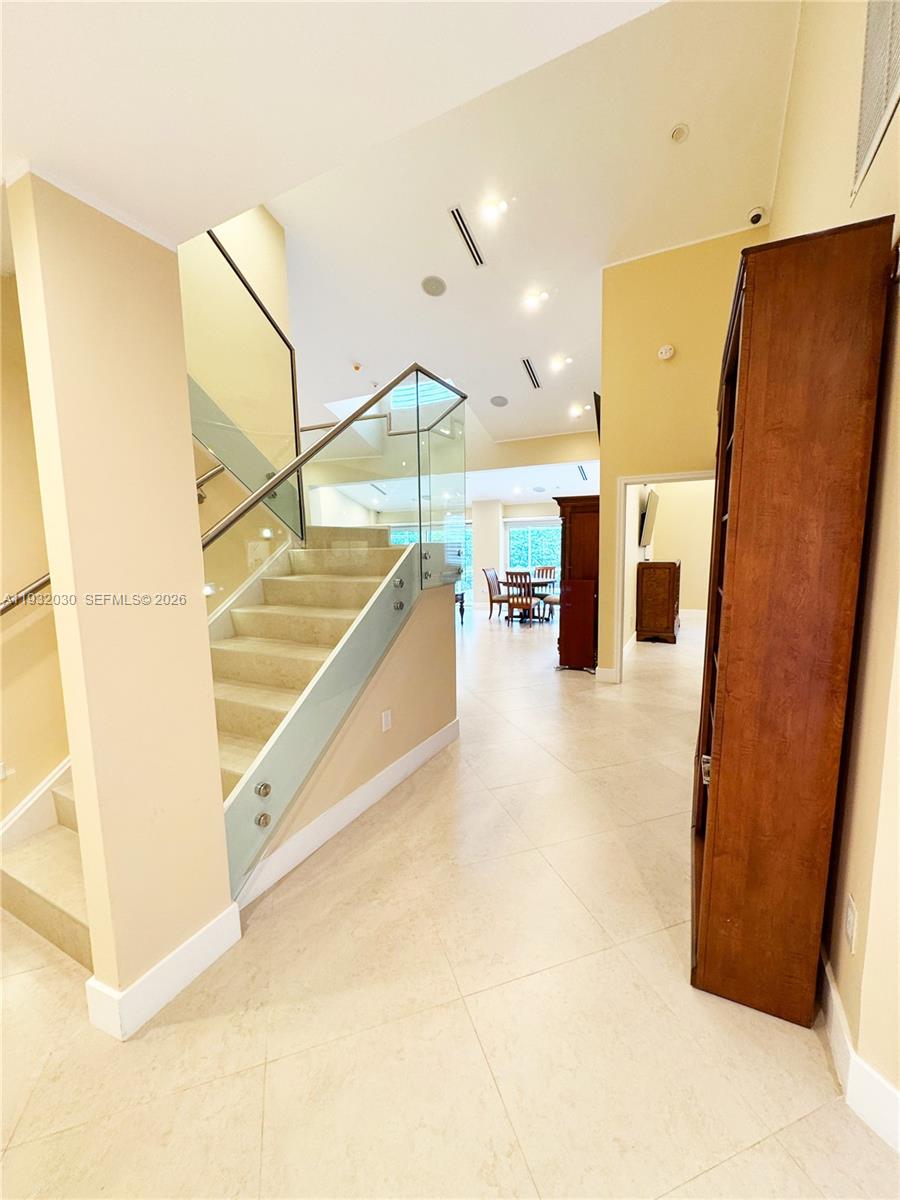 A staircase with glass railings leads to an upper level in a bright foyer — 610 Misty Oaks Ln, Pompano Beach FL 33069, POMPANO BEACH, FL