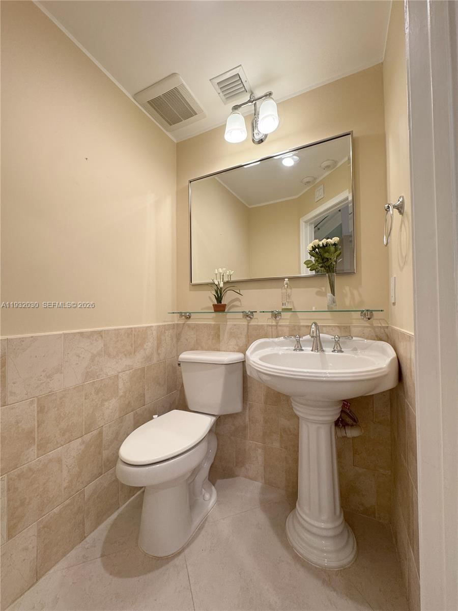 A bathroom features a pedestal sink, a toilet, and a mirror above a glass shelf — 610 Misty Oaks Ln, Pompano Beach FL 33069, POMPANO BEACH, FL
