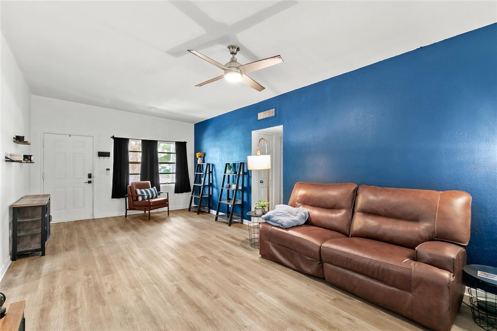 A living room features light wood-look flooring, a blue accent wall, and a brown leather sofa — 141 COUNTRY CLUB DRIVE, SANFORD, FL