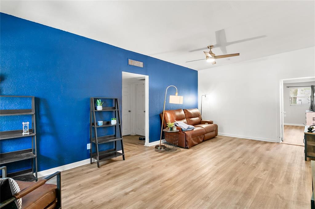 A living room features a bold blue accent wall, wood-look flooring, and brown leather furniture — 141 COUNTRY CLUB DRIVE, SANFORD, FL