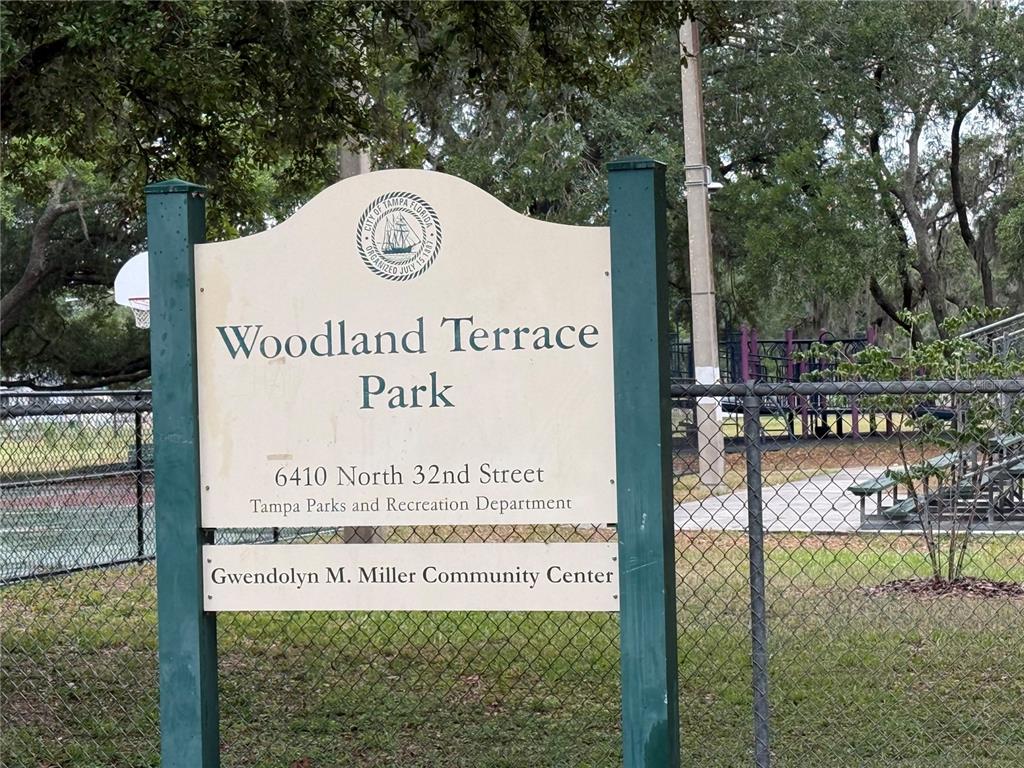 A sign for Woodland Terrace Park stands in front of a chain-link fence and playground — 3210 E FERN STREET, TAMPA, FL