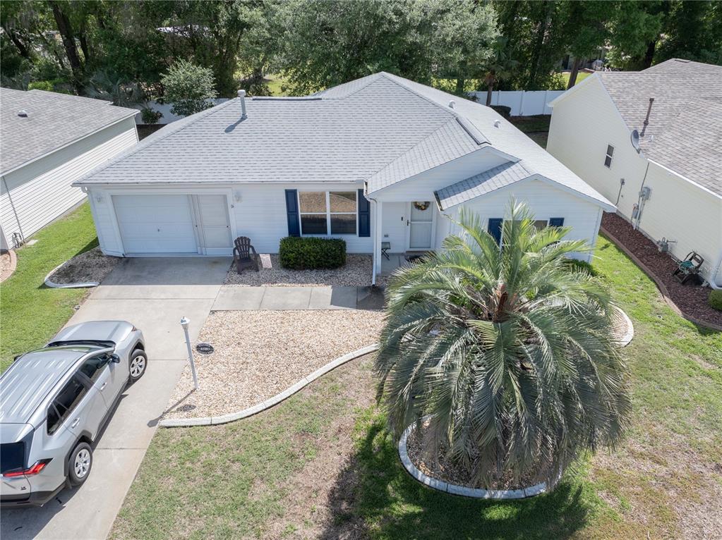 A single-story white house with blue shutters features a gravel yard and a concrete driveway — 16980 SE 96TH CHAPELWOOD CIRCLE, THE VILLAGES, FL