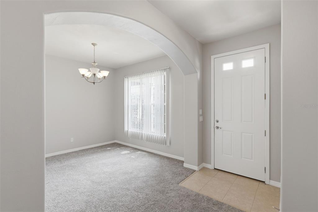 A dining room with gray carpet and a chandelier sits next to a tiled entryway — 3515 ROMEA CIRCLE, NEW SMYRNA BEACH, FL
