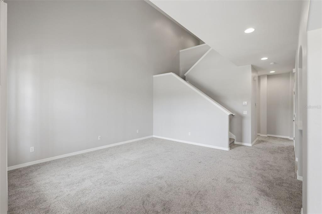 An empty room with gray carpeting, light gray walls, and a staircase leading upstairs — 3515 ROMEA CIRCLE, NEW SMYRNA BEACH, FL