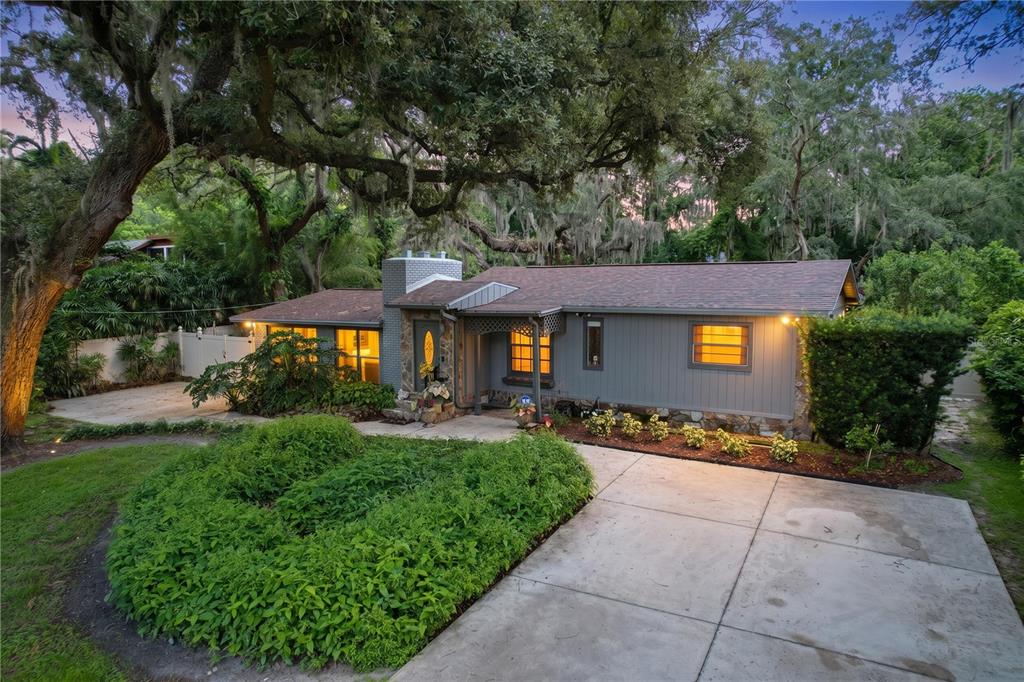 A single-story house with gray vertical siding, a stone chimney, and a concrete driveway — 11805 N 51ST STREET, TEMPLE TERRACE, FL