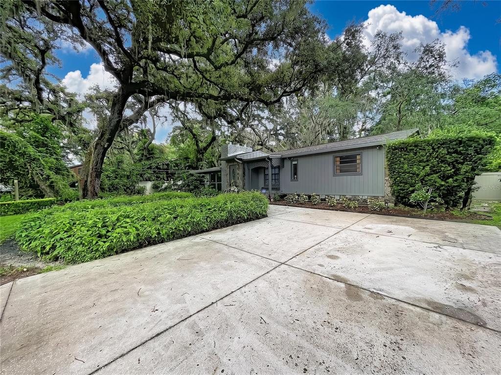 A gray single-story house with a concrete driveway sits beneath large, moss-covered oak trees — 11805 N 51ST STREET, TEMPLE TERRACE, FL