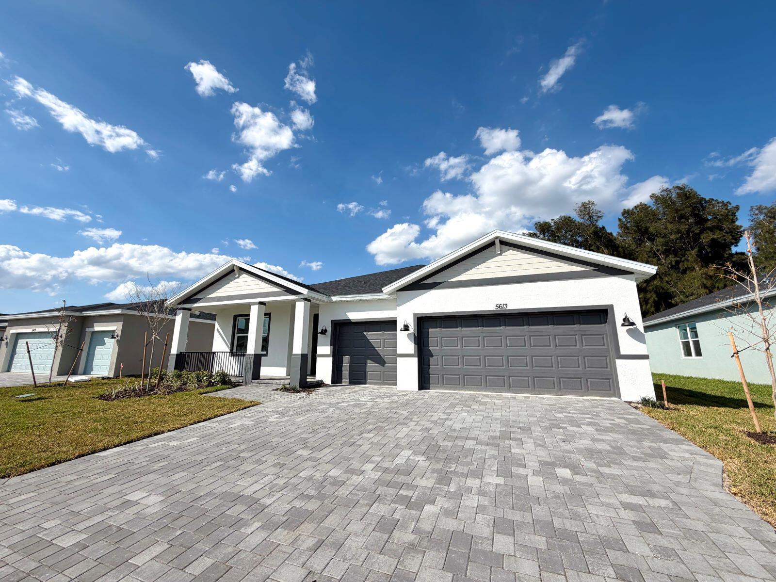 A single-story house with a white stucco exterior, gray garage doors, and a paver driveway — 5613 Hampton Park Circle, Vero Beach FL 32966, VERO BEACH, FL