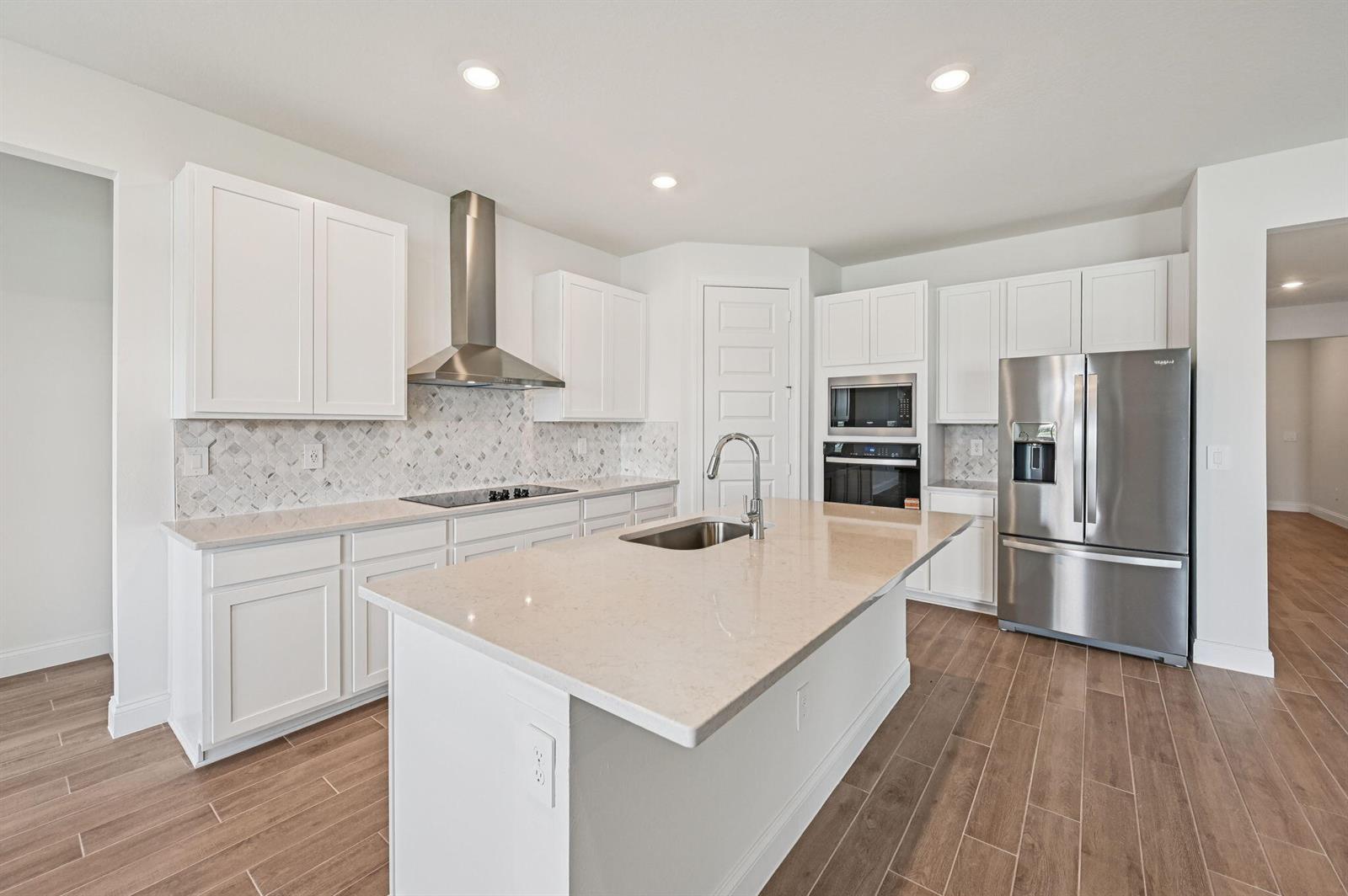 A modern kitchen features white cabinets, stainless steel appliances, a center island, and wood-look flooring — 5613 Hampton Park Circle, Vero Beach FL 32966, VERO BEACH, FL
