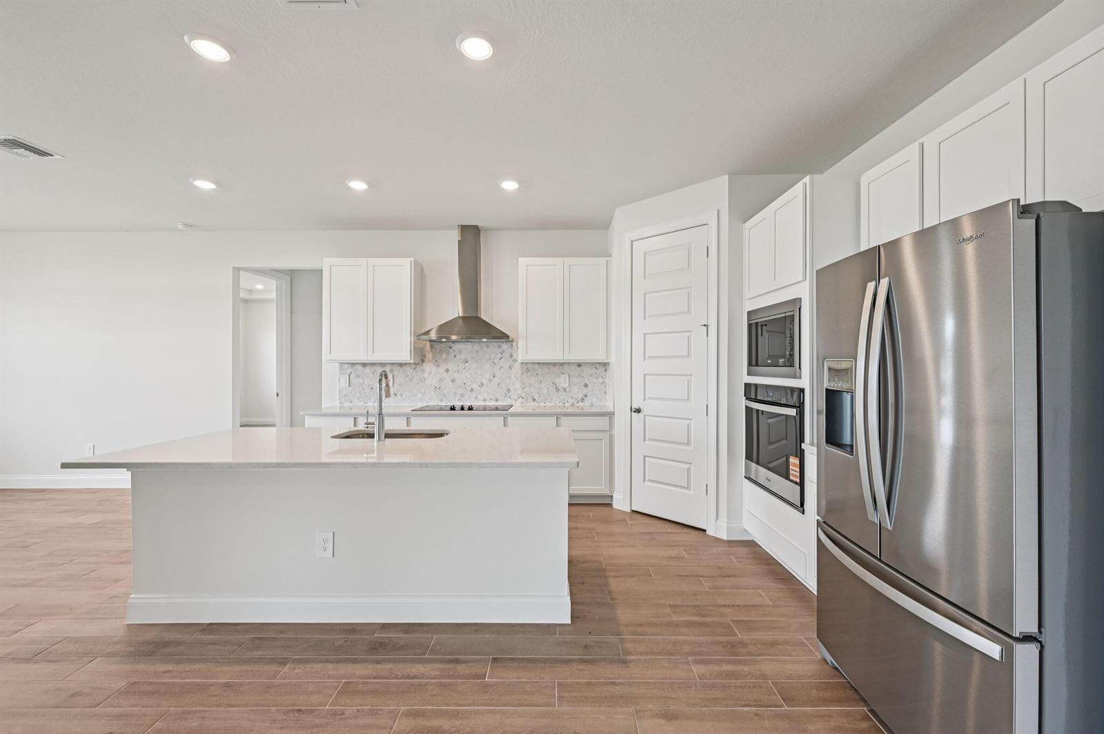 A modern kitchen features white cabinetry, stainless steel appliances, a center island, and wood-look flooring — 5613 Hampton Park Circle, Vero Beach FL 32966, VERO BEACH, FL