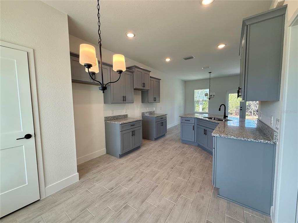 A kitchen features gray cabinets, granite countertops, and light wood-look tile flooring — 27204 DEEP CREEK BOULEVARD, PUNTA GORDA, FL