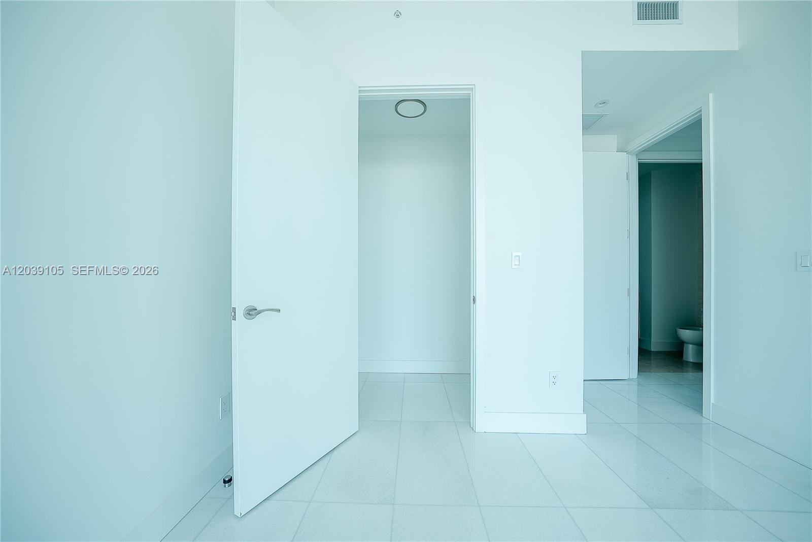 A white-walled room features a walk-in closet, a bathroom doorway, and tiled flooring — MIAMI, FL
