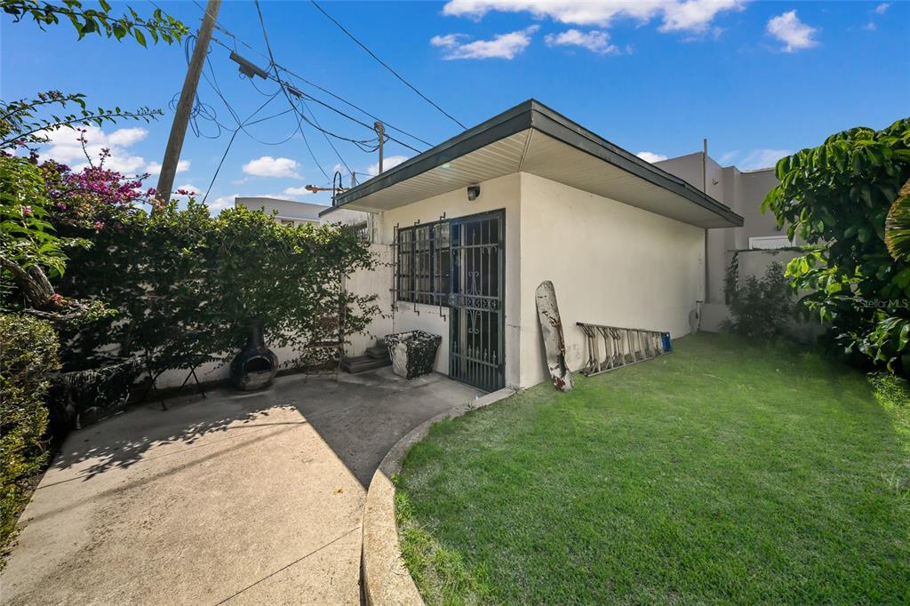 A small, flat-roofed building with a security door sits beside a concrete patio and lawn — 411 BURNS COURT, SARASOTA, FL