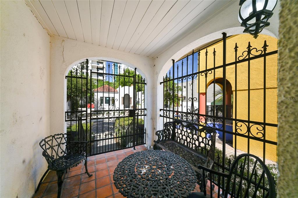 A covered patio features wrought iron furniture, tile flooring, and arched metal security gates — 411 BURNS COURT, SARASOTA, FL