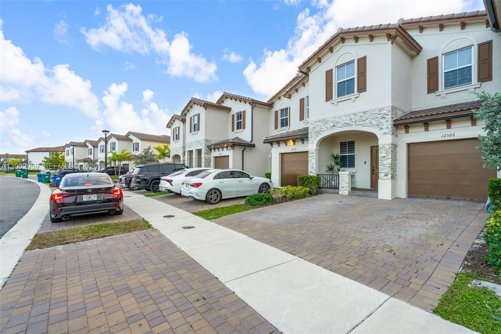 A row of two-story townhomes with paved driveways and parked cars under a blue sky — 12586 NW 22nd Pl, Miami FL 33167, MIAMI, FL