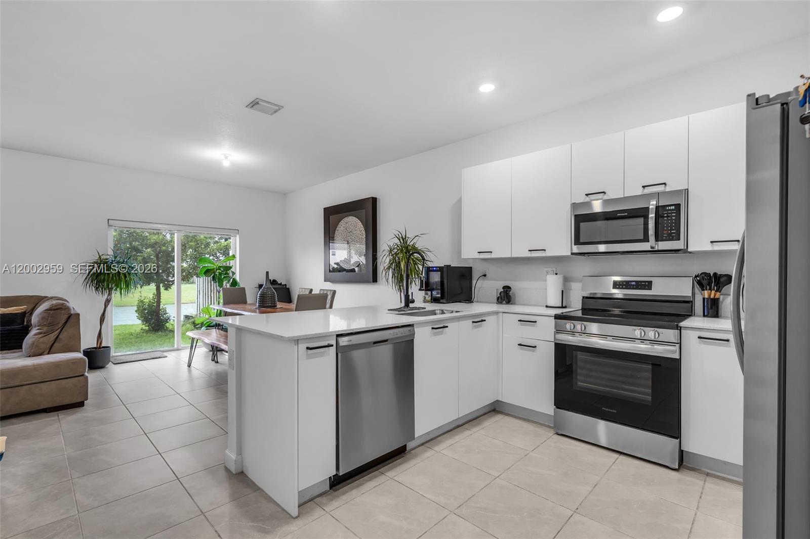 A modern kitchen with white cabinets and stainless steel appliances opens to a dining area — 12586 NW 22nd Pl, Miami FL 33167, MIAMI, FL