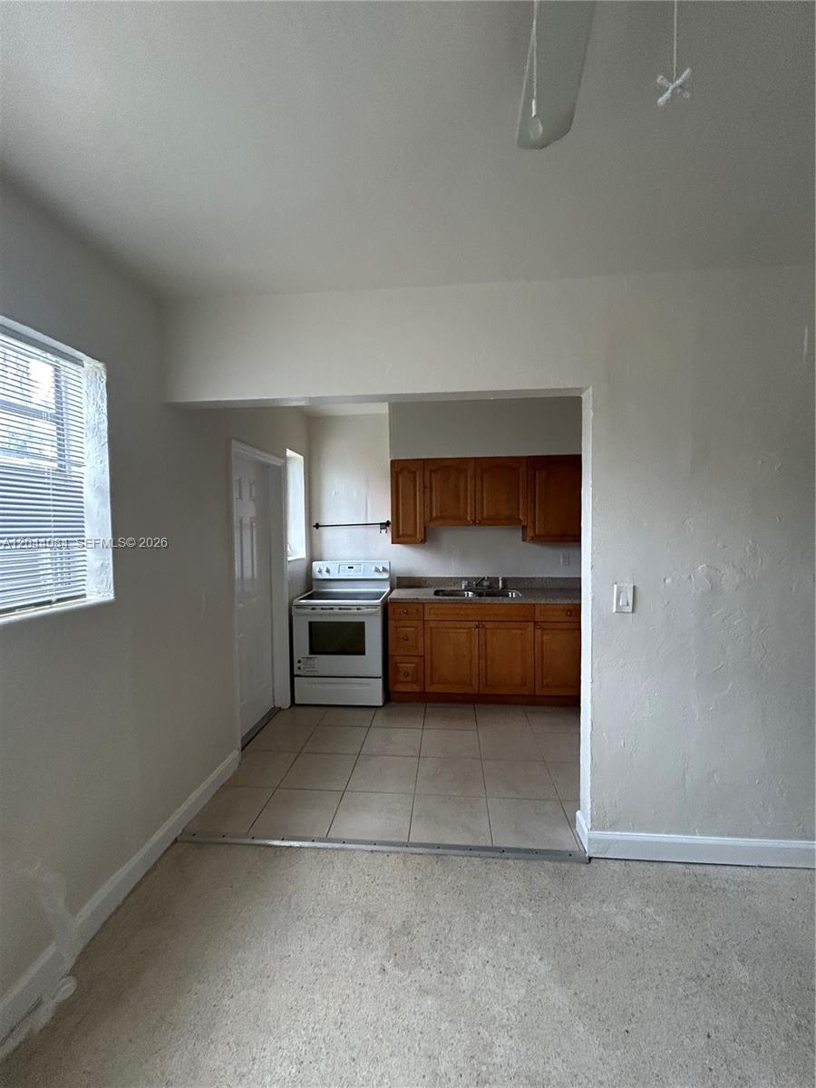 A small kitchen with wood cabinets and a white stove sits off a carpeted room — 730 83rd St # 2, Miami Beach FL 33141, MIAMI BEACH, FL