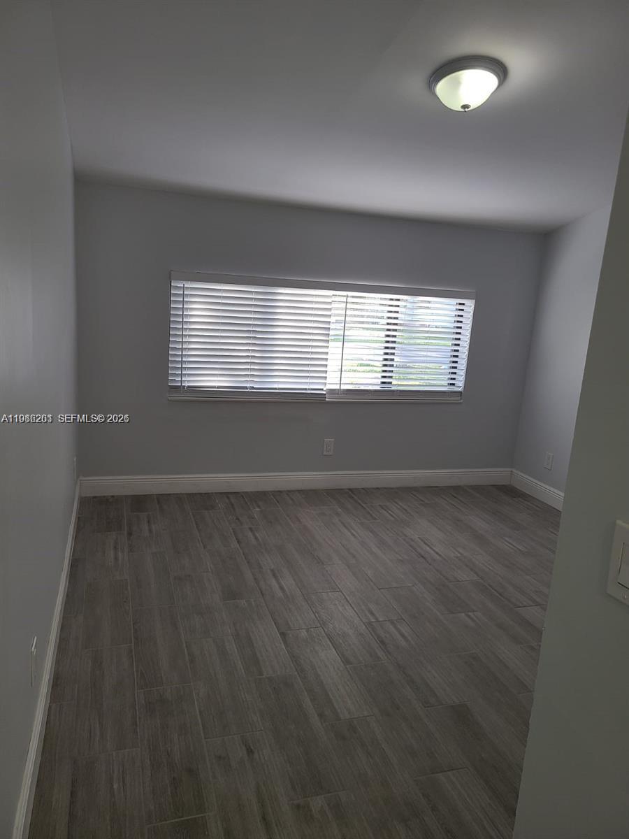 An empty room features light gray walls, wood-look tile flooring, and a window with blinds — 2008 NE 4th Ave # R, Wilton Manors FL 33305, WILTON MANORS, FL