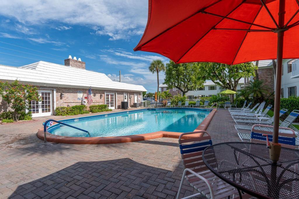 An outdoor swimming pool with lounge chairs and a red umbrella on a brick patio — 400 S Cypress Road # 404, Pompano Beach FL 33060, POMPANO BEACH, FL