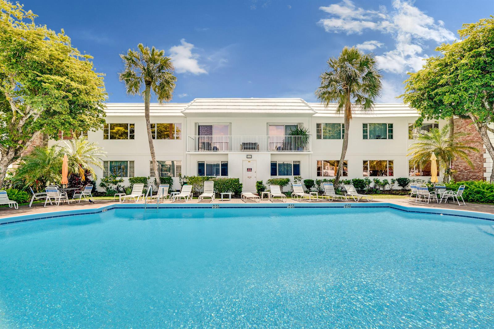 A two-story white building sits behind a large rectangular swimming pool with lounge chairs — 400 S Cypress Road # 404, Pompano Beach FL 33060, POMPANO BEACH, FL