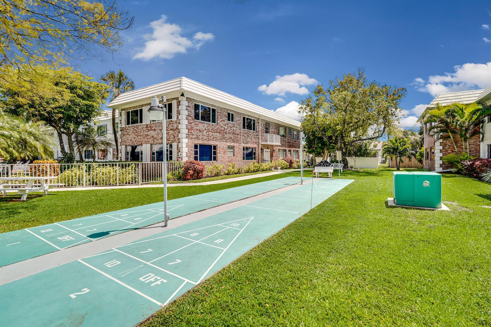 An outdoor shuffleboard court sits on a grassy lawn between two brick apartment buildings — 400 S Cypress Road # 404, Pompano Beach FL 33060, POMPANO BEACH, FL
