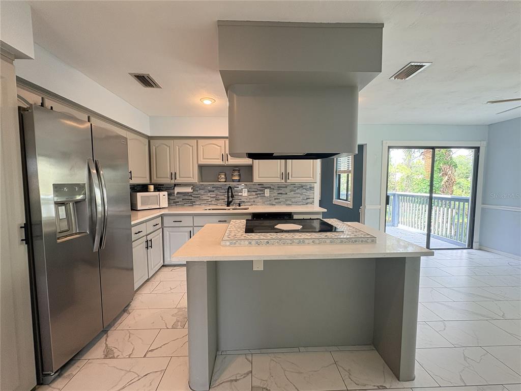 A kitchen features a central island with a cooktop, stainless steel appliances, and tiled flooring — 100 KINGBIRD CIRCLE UNIT 1, DAYTONA BEACH, FL
