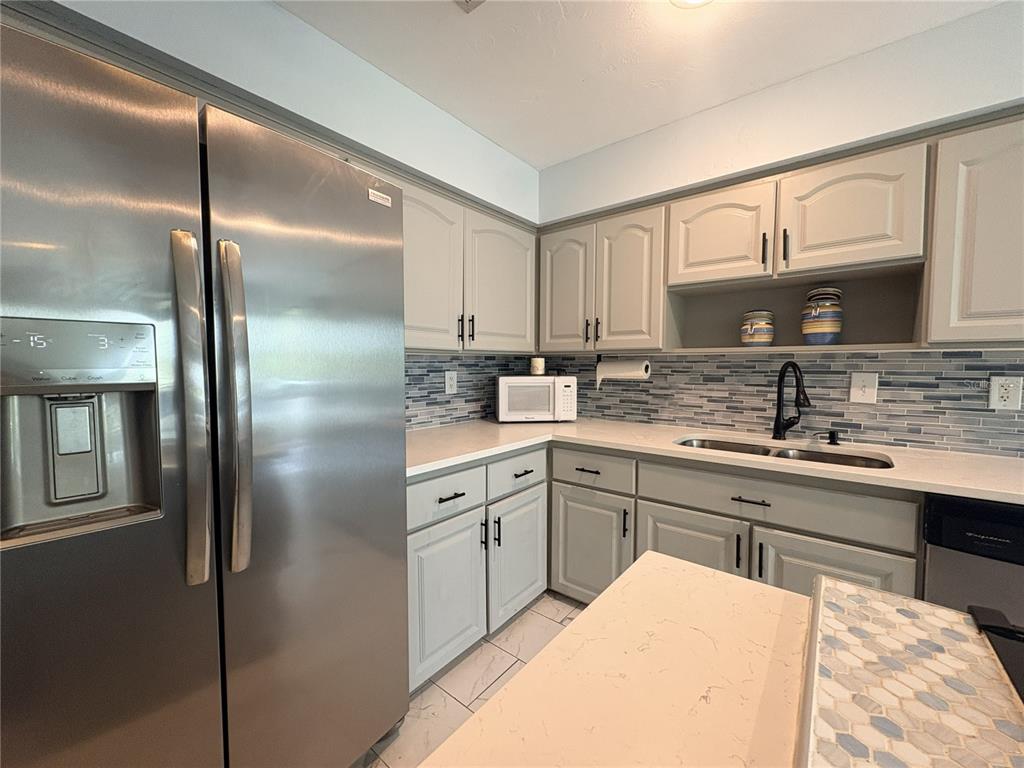 A kitchen features stainless steel appliances, light gray cabinets, and a blue glass tile backsplash — 100 KINGBIRD CIRCLE UNIT 1, DAYTONA BEACH, FL