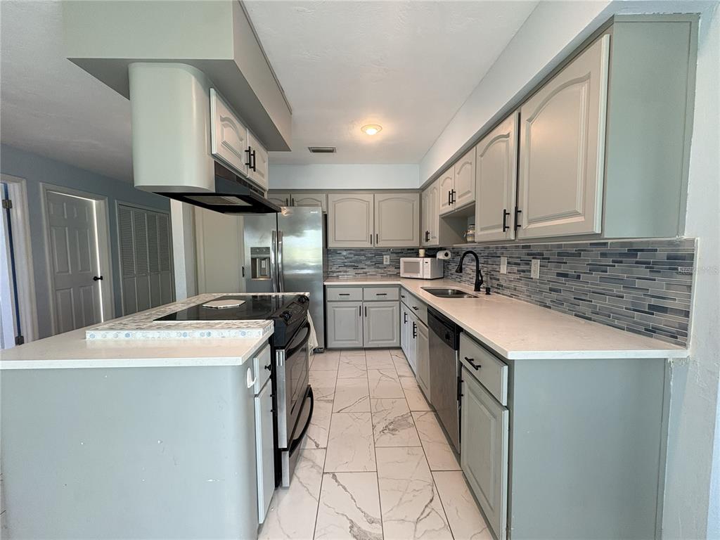A kitchen features gray cabinets, white countertops, a tiled backsplash, and a central island — 100 KINGBIRD CIRCLE UNIT 1, DAYTONA BEACH, FL