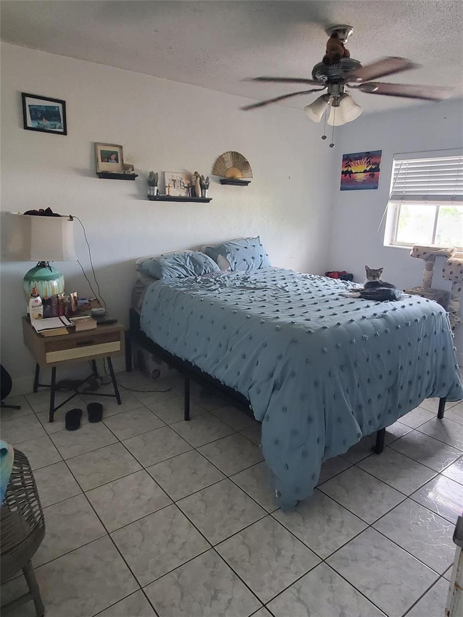 A bedroom features a bed with a blue textured comforter, tile flooring, and a ceiling fan — 1021 NE 24th Avenue # 30, Pompano Beach FL 33062, POMPANO BEACH, FL