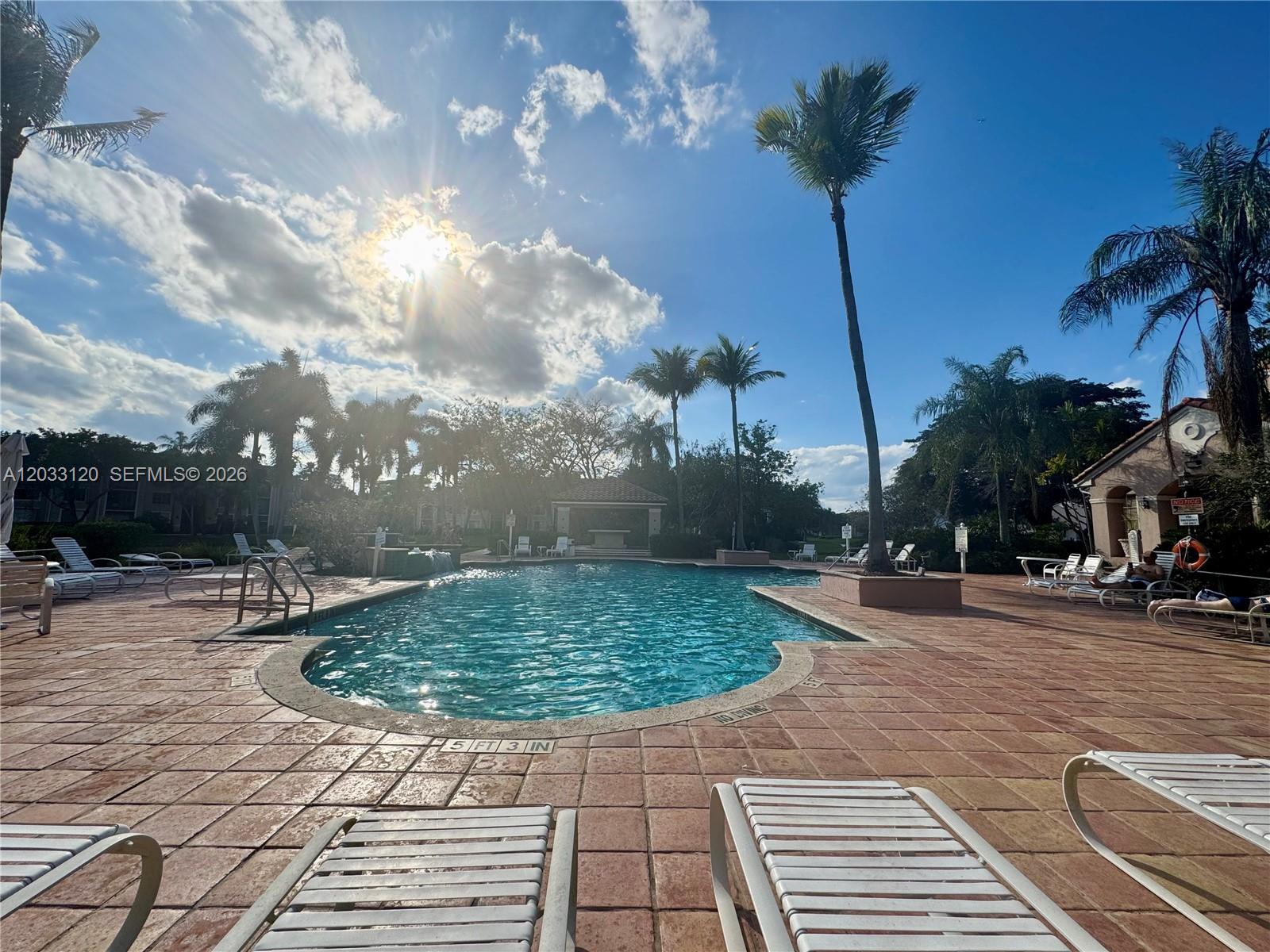 An outdoor swimming pool surrounded by a tiled deck, lounge chairs, and palm trees — 12142 Saint Andrews Pl # 107, Miramar FL 33025, MIRAMAR, FL