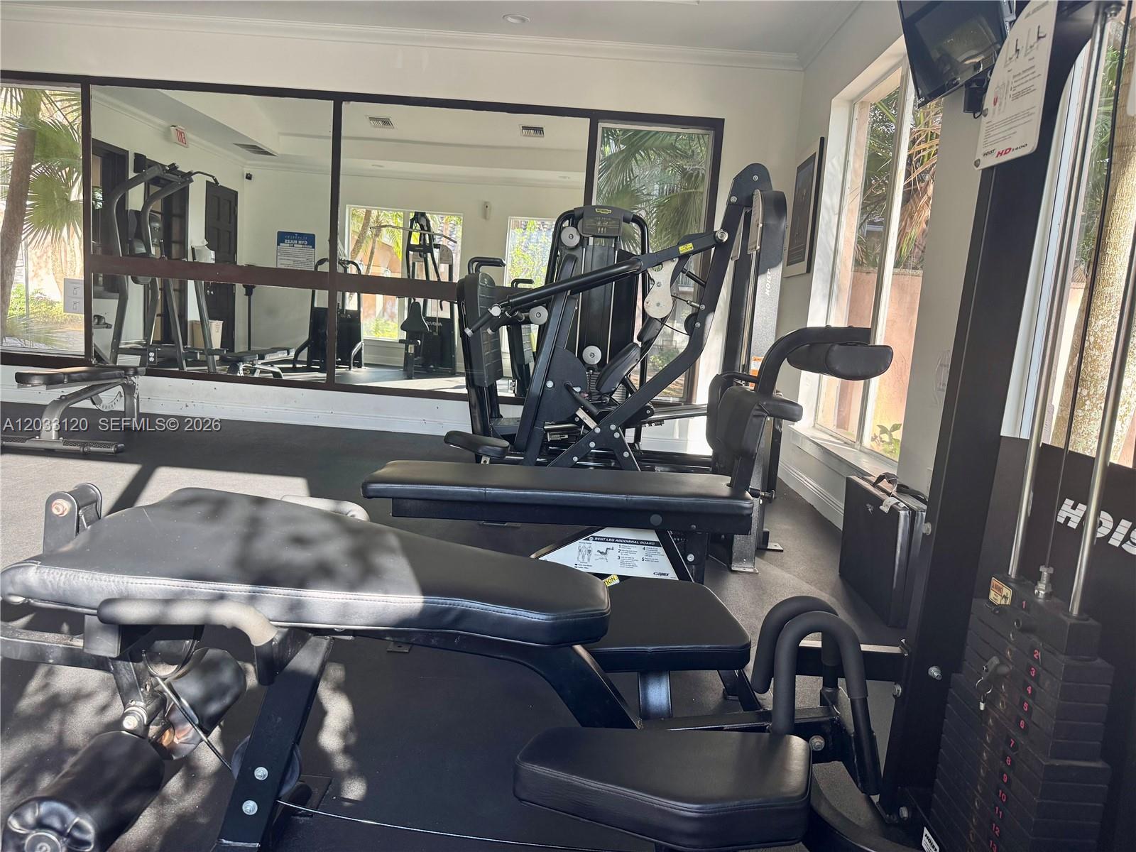 A gym room features black exercise equipment, a large wall mirror, and windows — 12142 Saint Andrews Pl # 107, Miramar FL 33025, MIRAMAR, FL