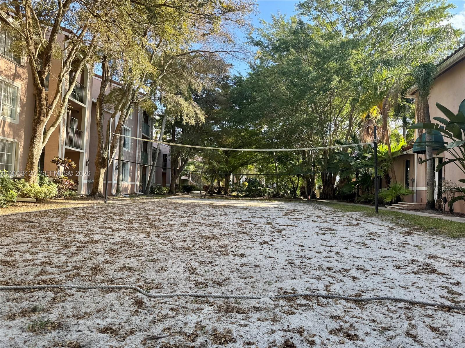 A sandy volleyball court sits between two residential apartment buildings surrounded by mature trees — 12142 Saint Andrews Pl # 107, Miramar FL 33025, MIRAMAR, FL