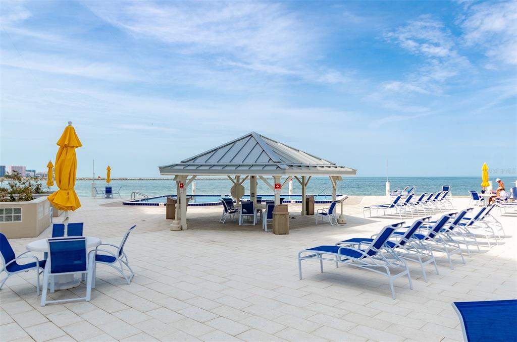 A poolside patio features a gazebo, lounge chairs, and tables overlooking the ocean — 450 S GULFVIEW BOULEVARD UNIT 405, CLEARWATER, FL